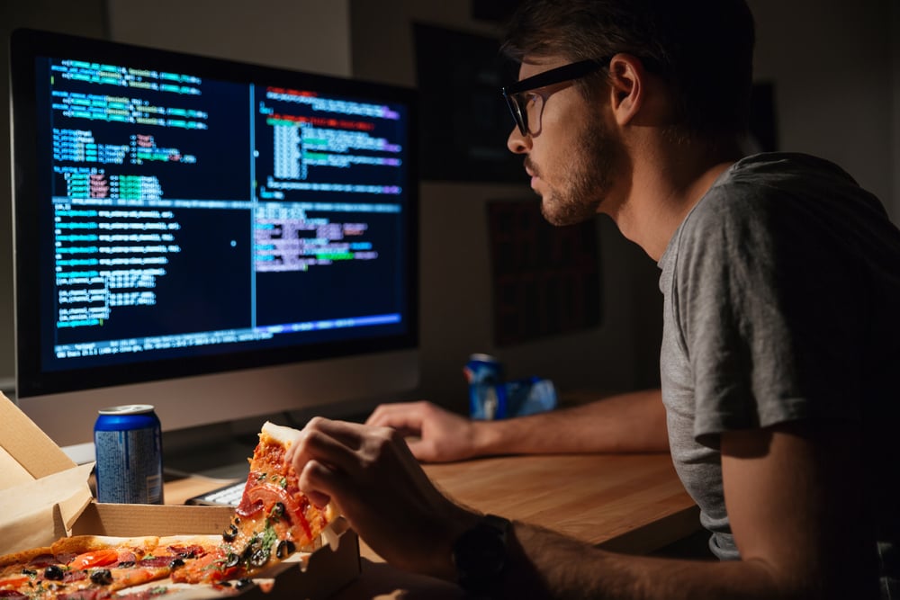 Perfil de un joven desarrollador de software concentrado que come pizza y codifica en casa