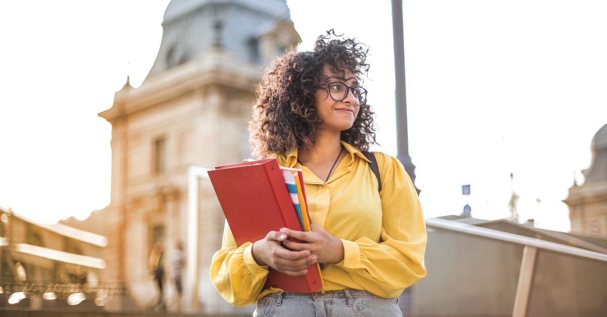 Estudiante con libros en la mano delante de un edificio universitario 